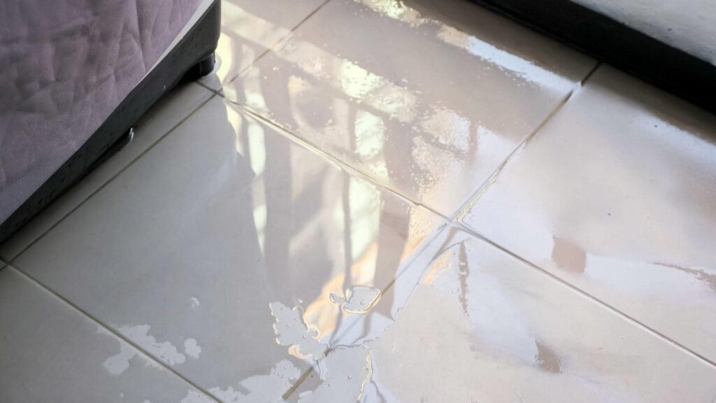 Water spilled on a tiled floor near the base of a bed.